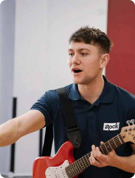 irock coach in blue shirt holding a guitar and teaching lessons